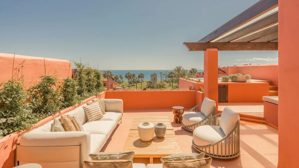 Terraza con muros de terracota, sofás y vistas al mar entre palmeras