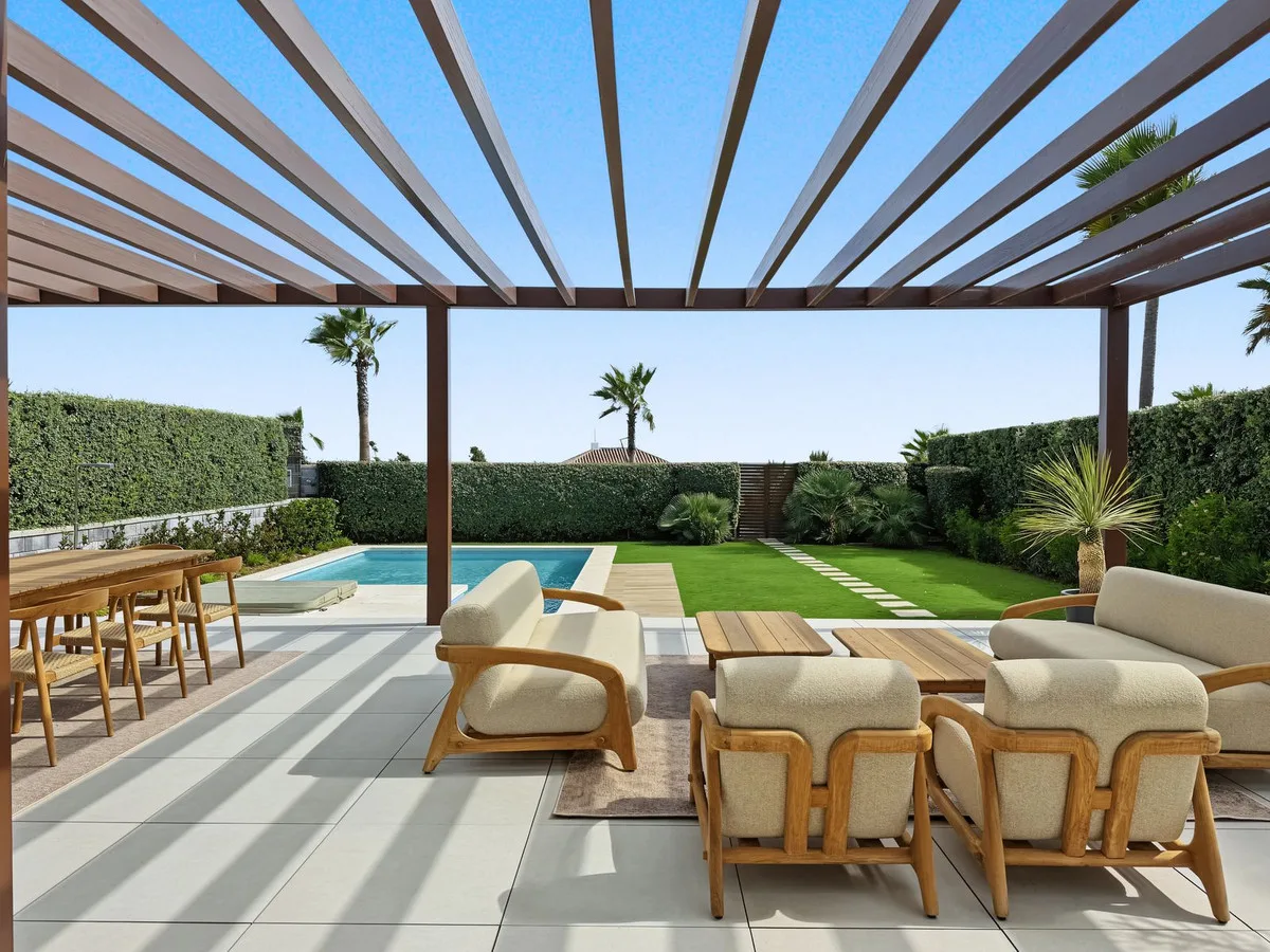 Terraza bajo una pérgola de madera, con butacas y jardín, en una villa de la New Golden Mile